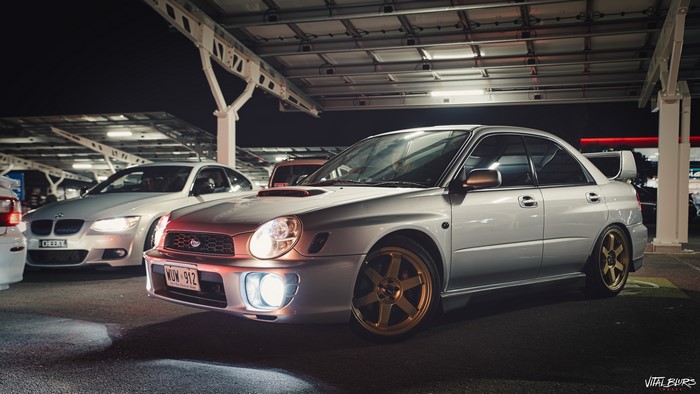Silver Subaru Impreza WRX with colored wheels at night