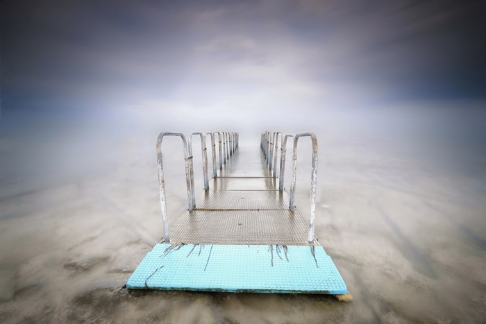A long pier with railings extends into a misty sea.