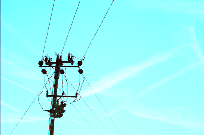 Telephone pole with transformer and wires against cyan sky