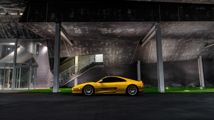 Yellow Ferrari F355 parked at modern building at night