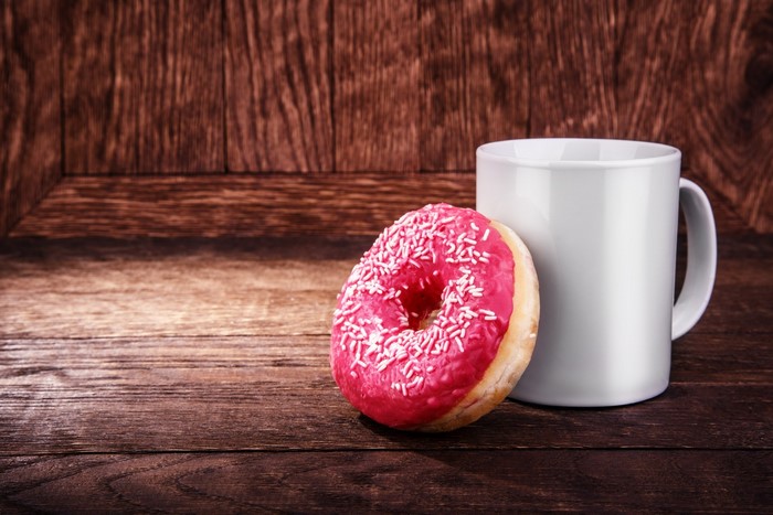 Pink frosted donut with sprinkles and a white mug