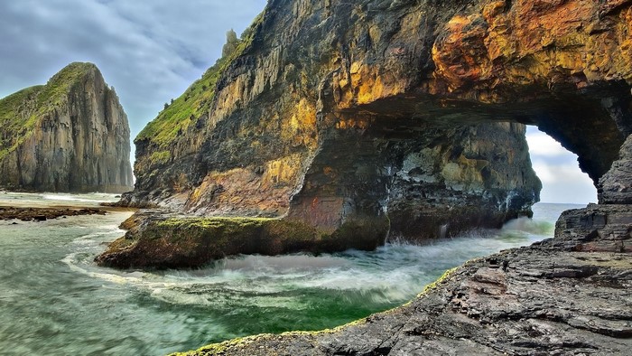 Archway rock formation with ocean waves and green hills