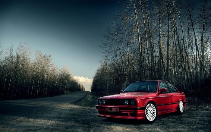 Red BMW E30 parked on a road next to trees