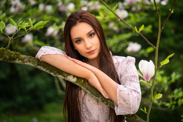 Brunette woman with long hair leaning on a tree branch