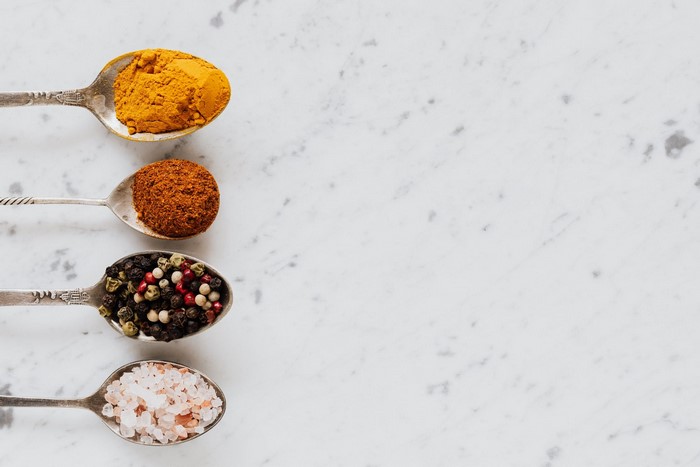 Four spoons with spices on a marble surface
