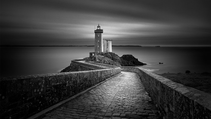 Monochrome landscape of a lighthouse on an island with a stone bridge