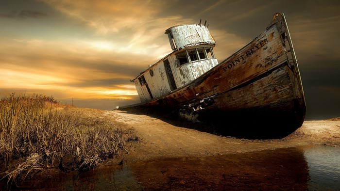 Wrecked boat named Point Reyes on a sandy shore at sunset