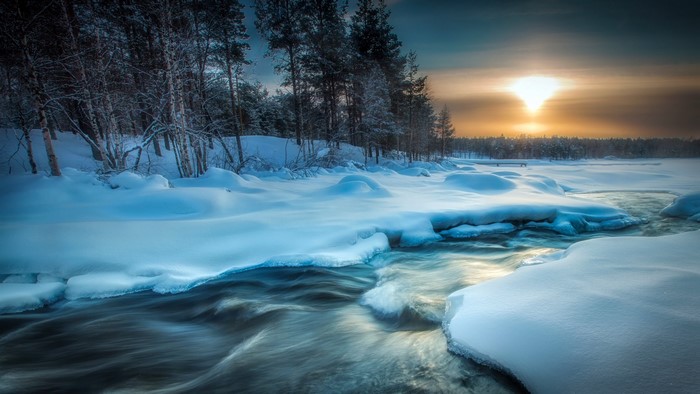 Winter river flowing through a snowy forest at sunset