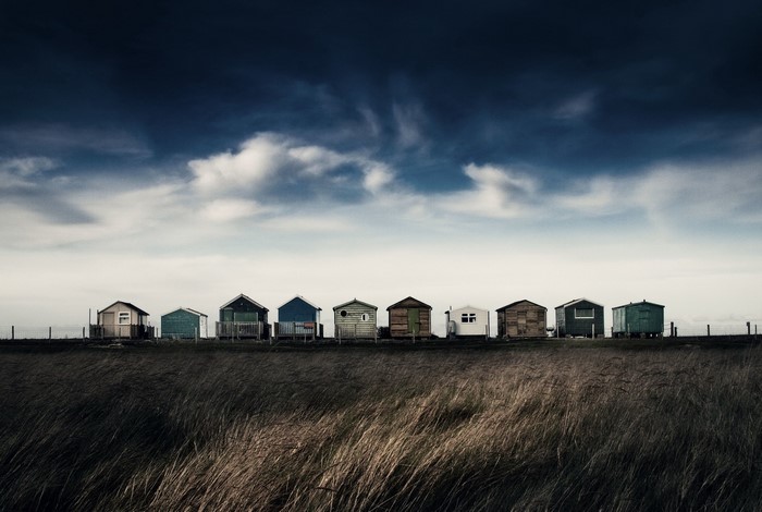 Beach huts lined up under a dramatic sky