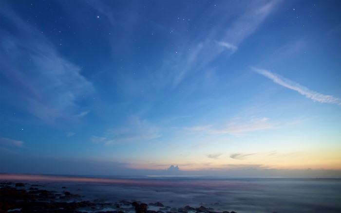 Night sky with stars over the ocean and rocks