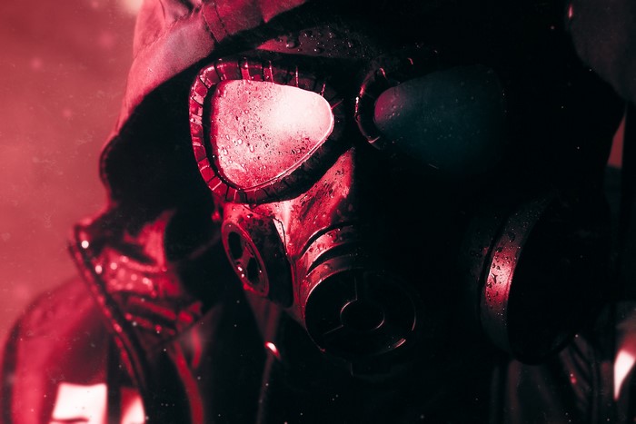 Person in gas mask and hood in red light