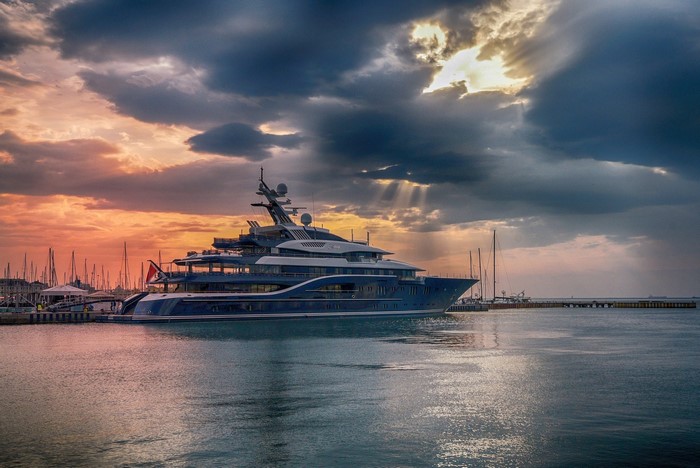 A large blue yacht docked in a harbor at sunset