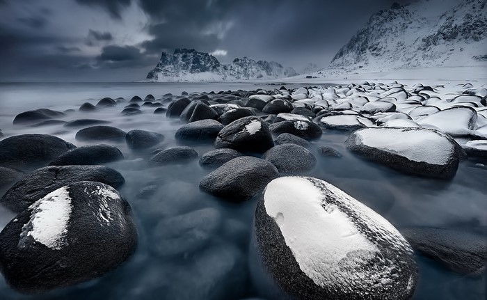 Snow-covered stones on a rocky coast with mountains