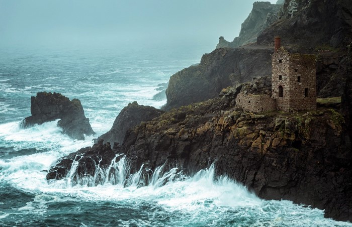 Ruined stone building on a rocky coast with crashing waves