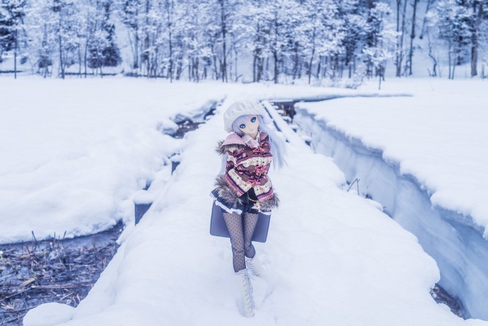 Anime doll in winter coat walking on a snowy bridge