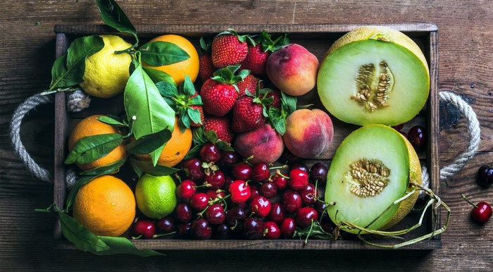 Tray of fresh fruits including strawberries, cherries, peaches, oranges, lemons, limes, and melons