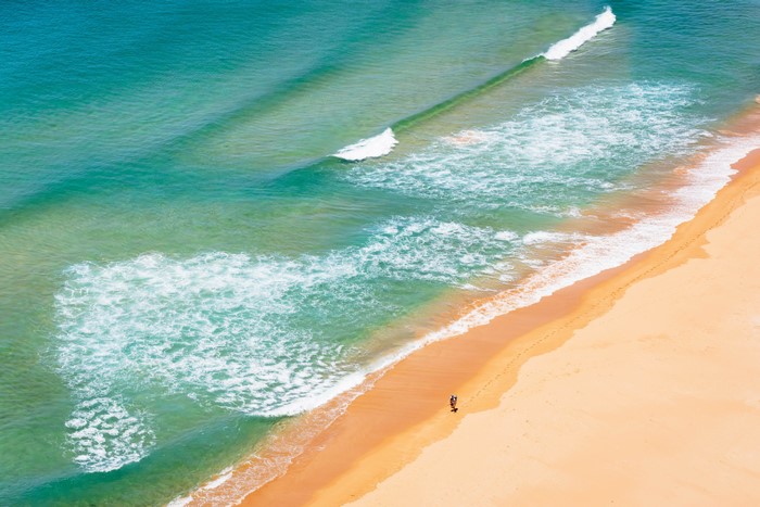 Aerial view of a beach with waves and two people walking