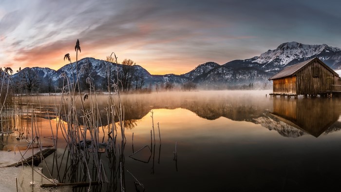 Wooden boathouse on a misty lake with snowy mountains