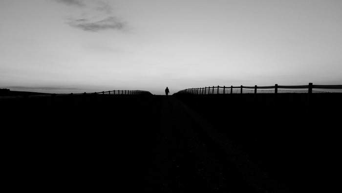 Silhouette of a person walking on a path with fences