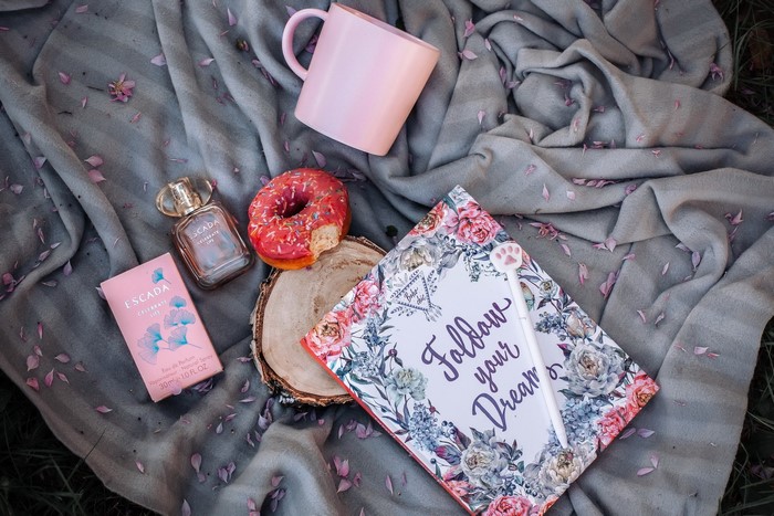 Escada perfume, donut, mug, and journal on blanket