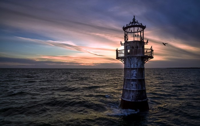 Lighthouse in the sea at sunset with birds