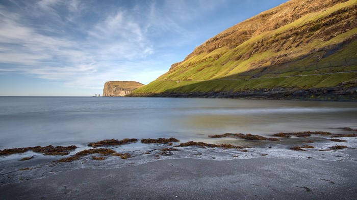 Beach with grassy cliffs and sea stacks in Faroe Islands
