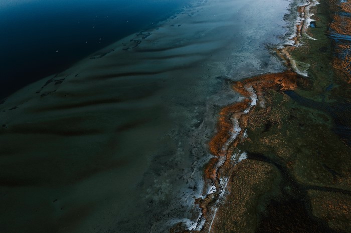Aerial view of a coastline with dark water and marshland