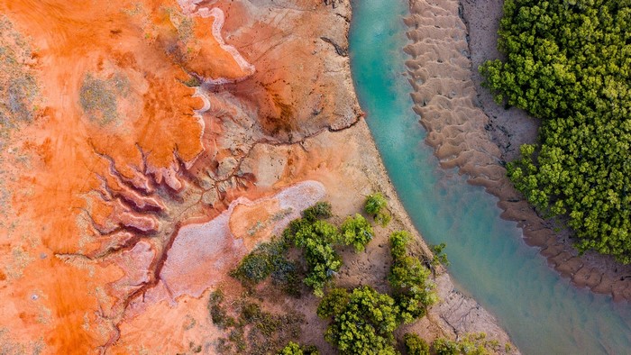 Aerial view of a river flowing through a landscape with red earth and green forest