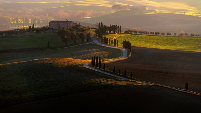 Tuscan landscape with winding road and farm at sunrise