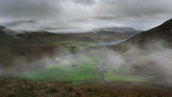 Misty valley with green fields and a lake