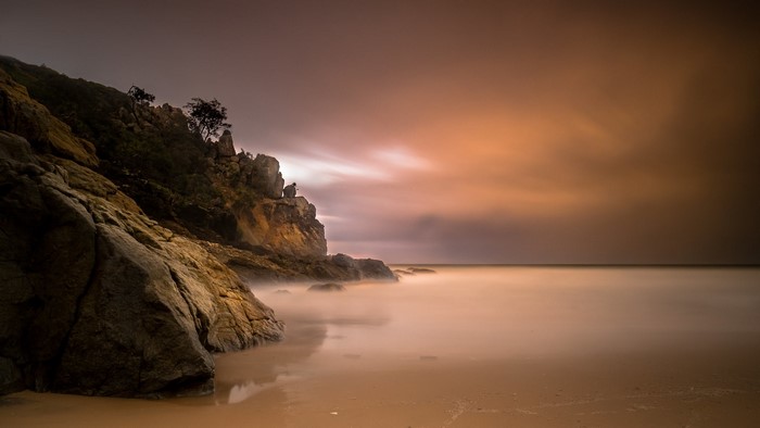 Long exposure of a rocky shore with misty sea and orange sky