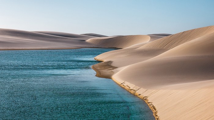 Desert dunes and turquoise water under a clear sky