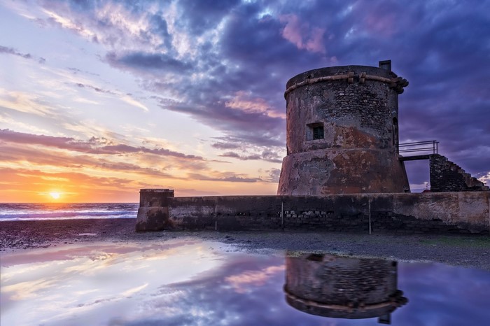 Old stone tower by the sea at sunset with reflection