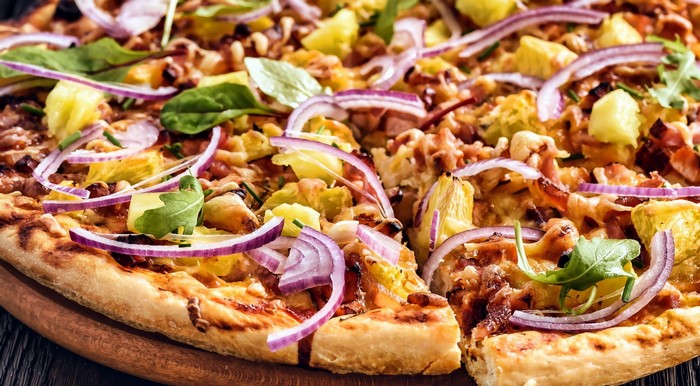 Pizza with pineapple, red onion, and greens