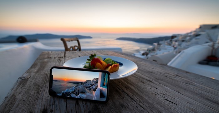 Smartphone displaying Santorini sunset over food on table