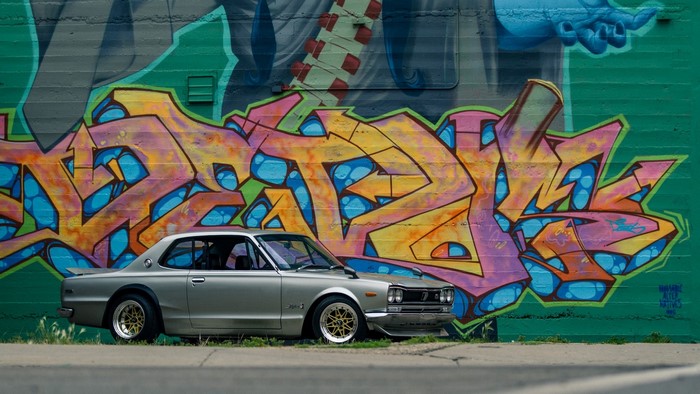 Silver Nissan Skyline C10 Hakosuka parked by graffiti wall