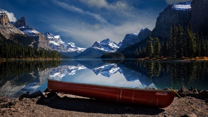 Red canoe on a rocky shore with mountains and lake reflection