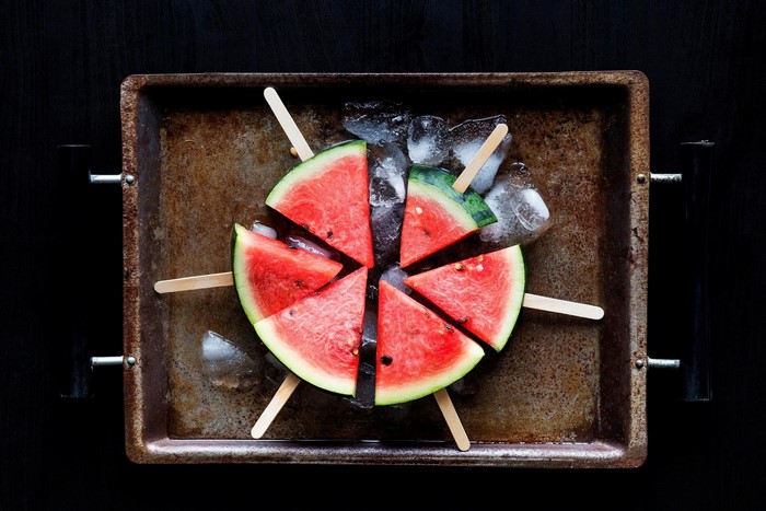 Watermelon slices on sticks with ice on a tray