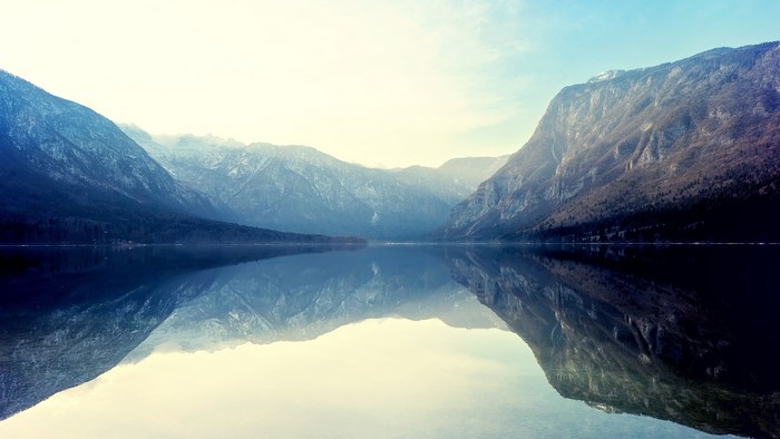 Mountains reflected in a calm lake under a bright sky