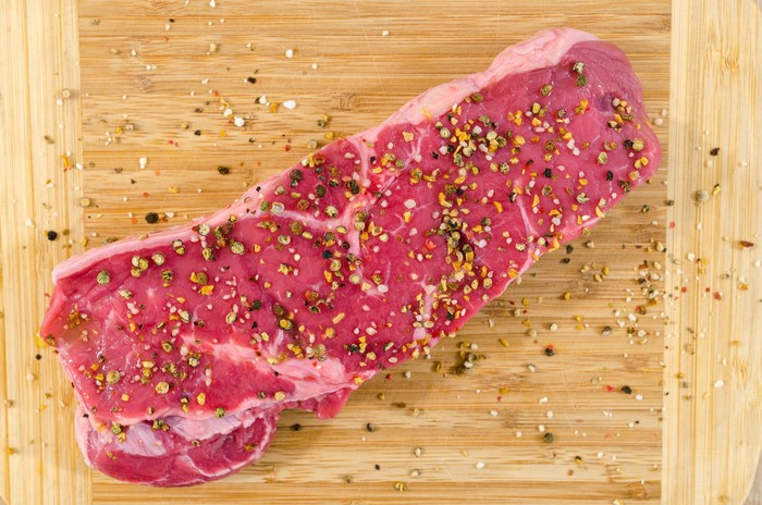 Raw beef steak seasoned with pepper on a cutting board