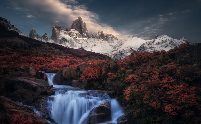 Waterfall and autumn trees with snow-capped mountains