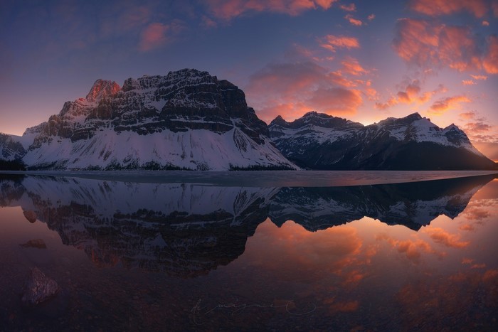 Snowy mountains reflected in a calm lake at sunset