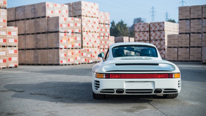 White Porsche 959 sports car in front of stacked pallets