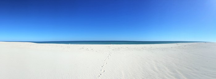 Footprints on a white sand beach with blue sky and sea