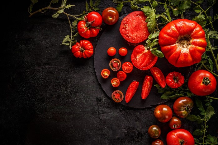Assortment of fresh tomatoes and leaves on a dark surface