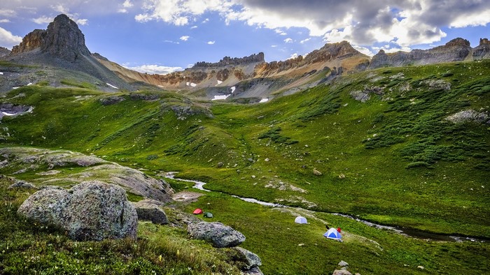 Tents in a mountain valley with stream and rocky peaks