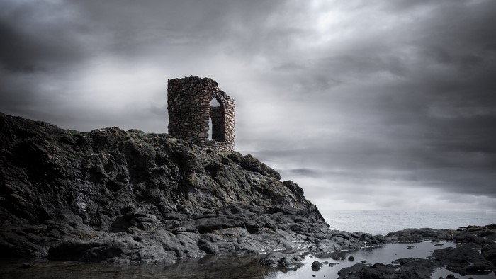 Stone ruin on a rocky coast under a cloudy sky