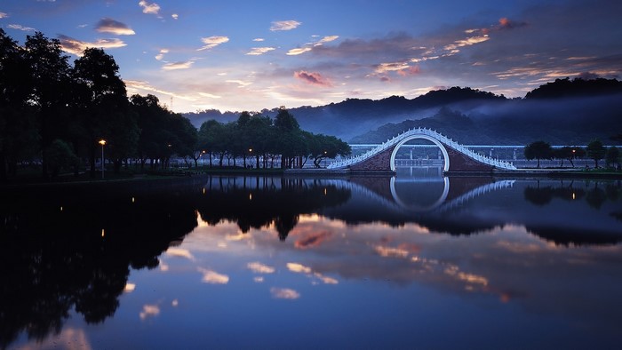 Arch bridge over water at dawn with misty mountains