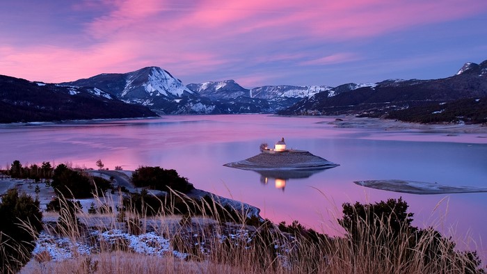 Chapel on an island in a lake with snowy mountains and pink sky
