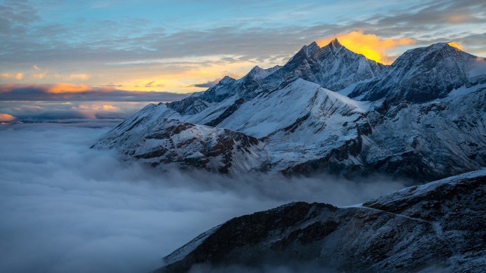 Snowy mountains in the Alps at sunset with clouds